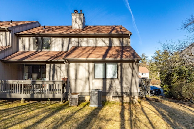 back of property featuring roof with shingles, a lawn, a chimney, a deck, and driveway