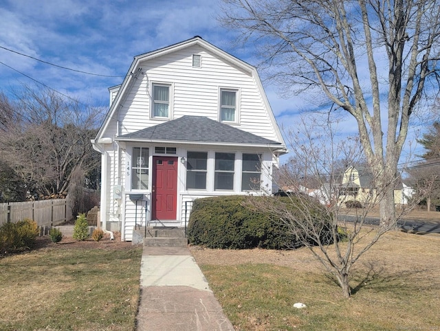 colonial inspired home with a gambrel roof, a shingled roof, a front yard, and fence