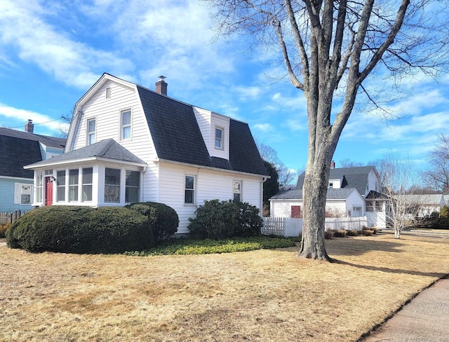 view of side of home with a shingled roof, fence, a gambrel roof, a lawn, and a chimney