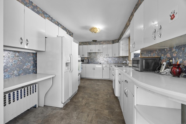 kitchen with radiator, white refrigerator with ice dispenser, white cabinetry, stainless steel microwave, and tasteful backsplash