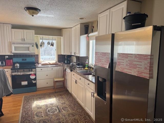 kitchen with wood finished floors, white cabinetry, stainless steel appliances, and a sink