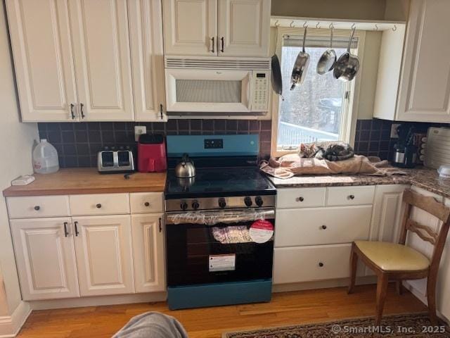 kitchen with white microwave, backsplash, stainless steel electric range oven, light wood-style floors, and white cabinetry