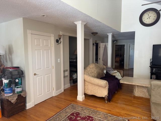 living area with baseboards, a textured ceiling, wood finished floors, and ornate columns