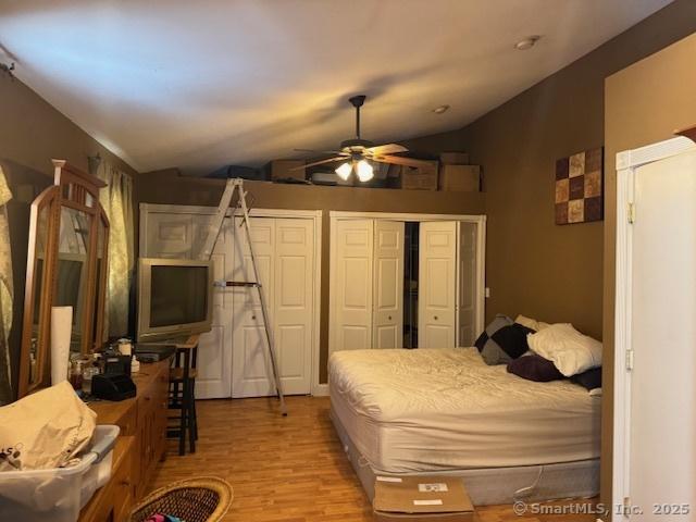 bedroom with multiple closets, lofted ceiling, and wood finished floors