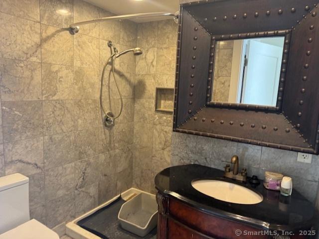 full bathroom featuring a tile shower, toilet, vanity, and tile walls