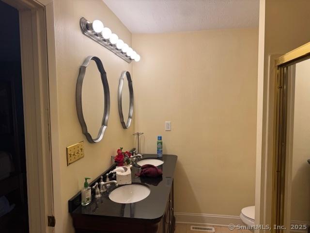 full bathroom with visible vents, baseboards, toilet, a shower with shower door, and vanity