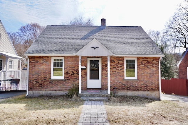 bungalow-style house featuring fence, brick siding, roof with shingles, and a chimney