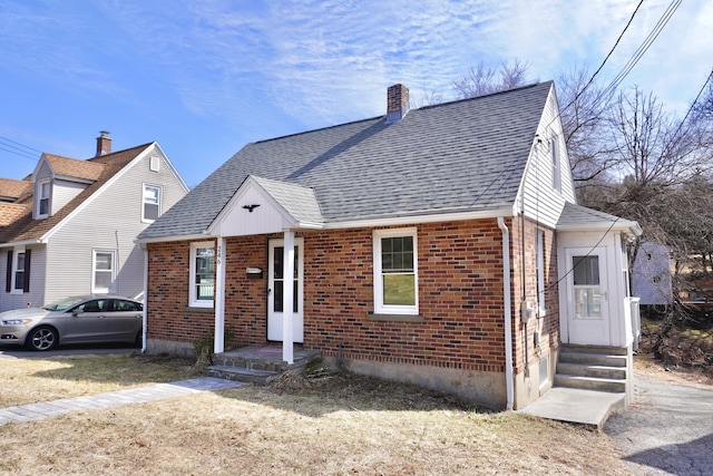 view of front of home with a front lawn, brick siding, a chimney, and a shingled roof