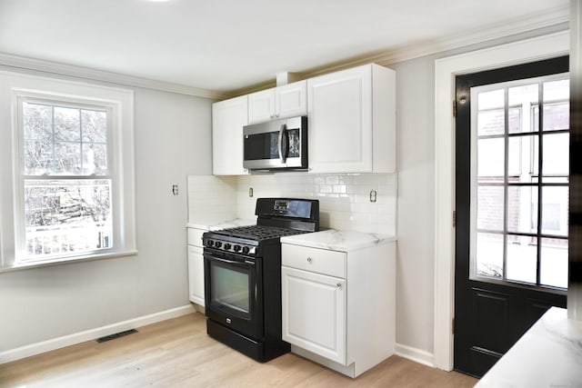 kitchen featuring visible vents, stainless steel microwave, black gas stove, white cabinets, and decorative backsplash