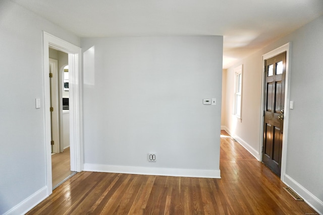 spare room with dark wood-type flooring, visible vents, and baseboards