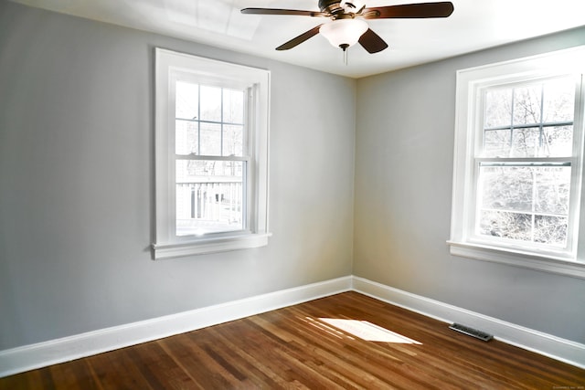 spare room with dark wood-type flooring, a healthy amount of sunlight, visible vents, and baseboards