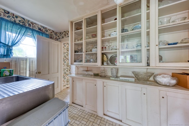 673 Spring St, Manchester, CT 06040 - kitchen with white cabinetry, light countertops, glass insert cabinets, wallpapered walls, and brick patterned floors