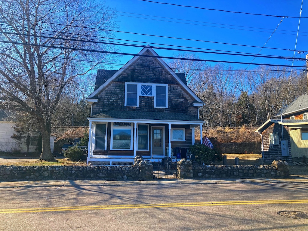 view of front of property featuring covered porch, a fenced front yard, and a shingled roof