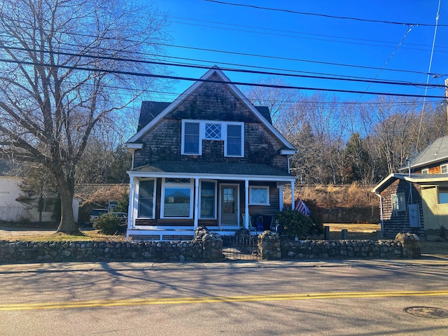 view of front of property featuring covered porch, a fenced front yard, and a shingled roof