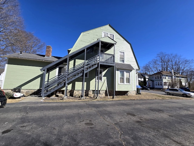 view of front facade featuring stairway, a gambrel roof, and a chimney