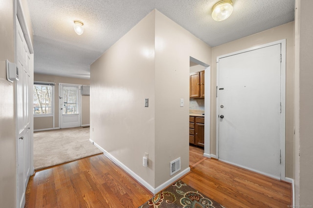 foyer entrance with baseboards, visible vents, light wood finished floors, and a textured ceiling