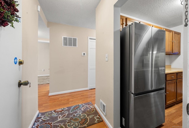 kitchen with light wood-type flooring, visible vents, brown cabinets, and freestanding refrigerator