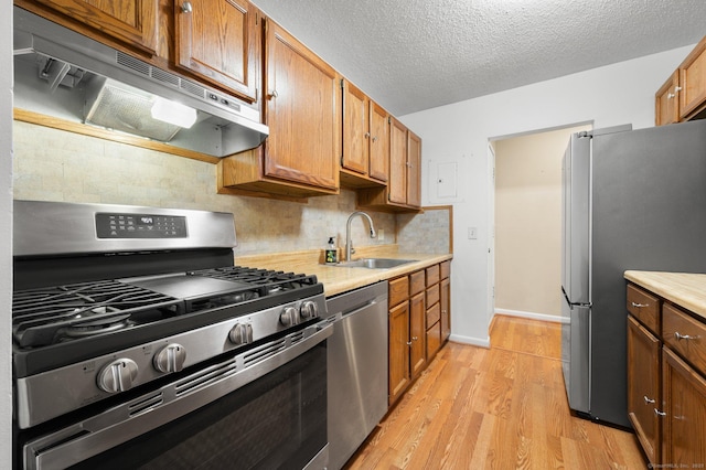 kitchen with under cabinet range hood, stainless steel appliances, a sink, and light countertops