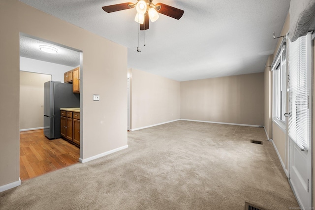 empty room with visible vents, ceiling fan, baseboards, light carpet, and a textured ceiling