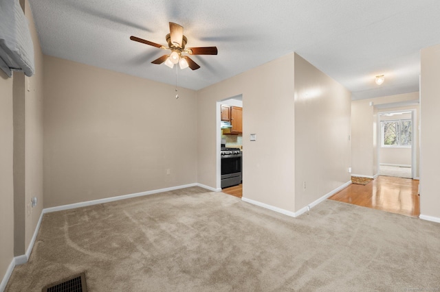 unfurnished living room with ceiling fan, light colored carpet, visible vents, and baseboards