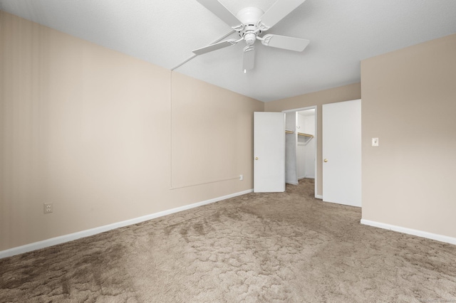 unfurnished bedroom with a spacious closet, baseboards, carpet floors, a closet, and a ceiling fan