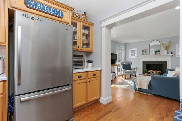 kitchen featuring light wood finished floors, a fireplace, freestanding refrigerator, light countertops, and glass insert cabinets