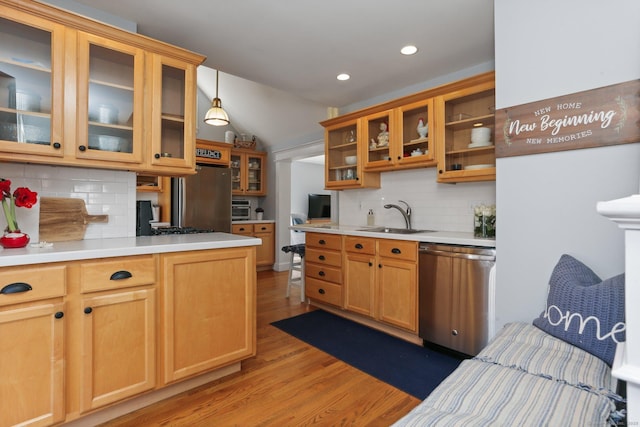 kitchen with glass insert cabinets, light countertops, appliances with stainless steel finishes, wood finished floors, and a sink