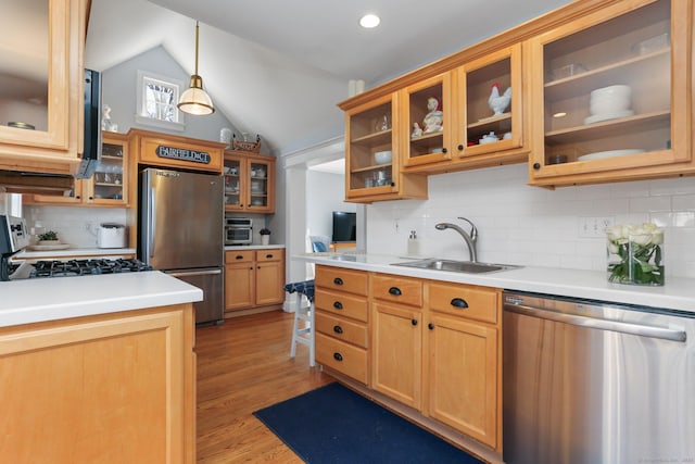 kitchen featuring lofted ceiling, a sink, stainless steel appliances, light countertops, and glass insert cabinets