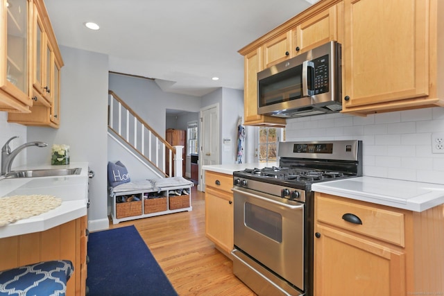 kitchen with light wood-type flooring, a sink, tasteful backsplash, stainless steel appliances, and light countertops