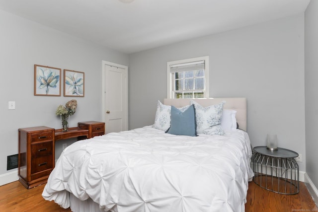 bedroom with wood finished floors, visible vents, and baseboards