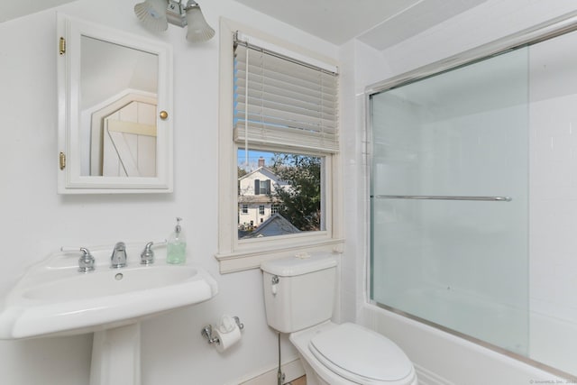 bathroom featuring a sink, toilet, and bath / shower combo with glass door