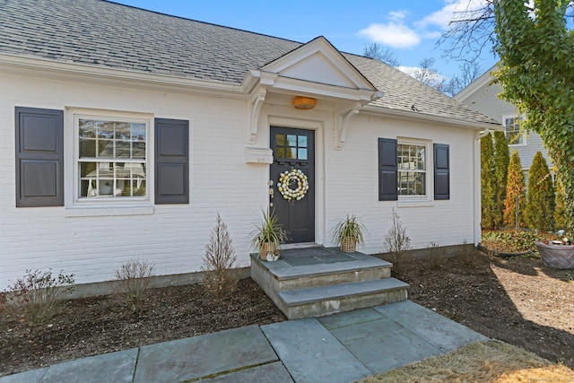 property entrance featuring brick siding and a shingled roof