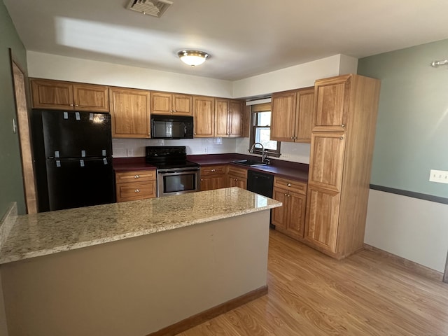 kitchen with light wood finished floors, visible vents, dark stone countertops, black appliances, and a sink