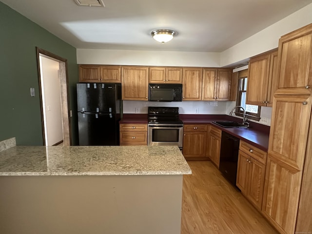 kitchen featuring a peninsula, light wood-style flooring, a sink, black appliances, and brown cabinets