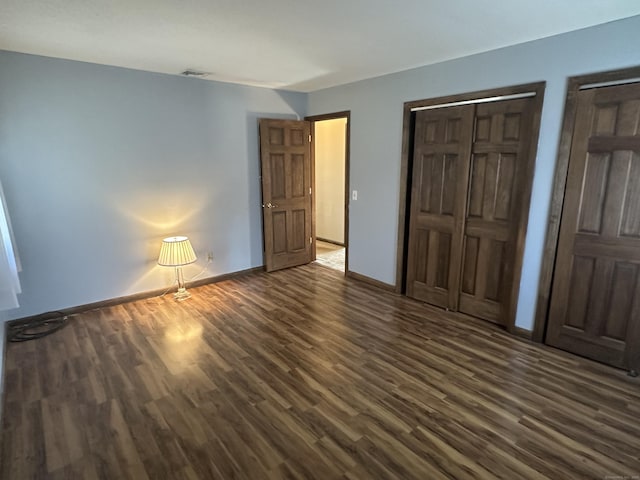 unfurnished bedroom featuring dark wood-type flooring, baseboards, visible vents, and a closet