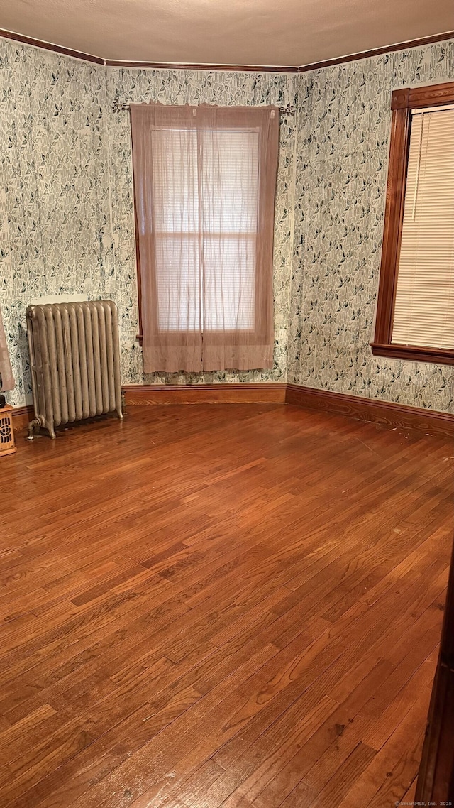 unfurnished room with ornamental molding, wood finished floors, wallpapered walls, and radiator