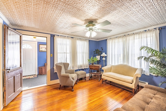 living area featuring crown molding, light wood-type flooring, an ornate ceiling, a ceiling fan, and a baseboard radiator