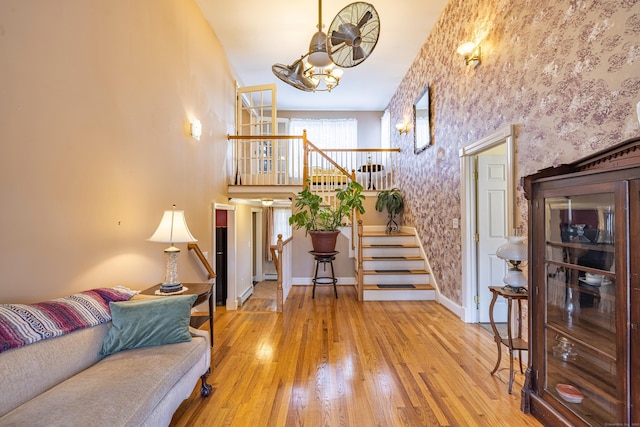 living area featuring stairway, wood-type flooring, a high ceiling, wallpapered walls, and baseboards