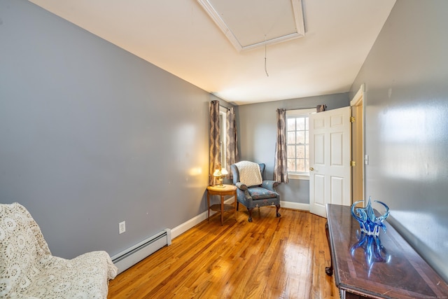 sitting room with light wood-type flooring, a baseboard radiator, baseboards, and attic access