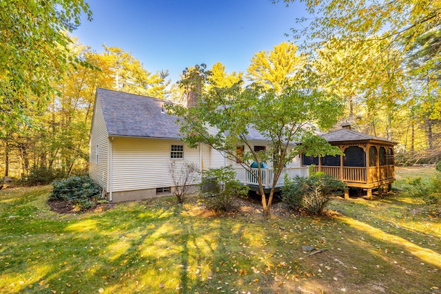 back of house with a wooden deck, roof with shingles, a gazebo, a lawn, and a chimney