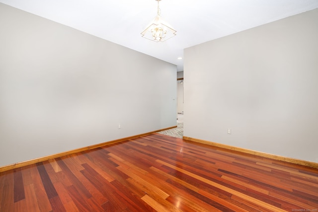 unfurnished room with a chandelier, baseboards, and wood finished floors