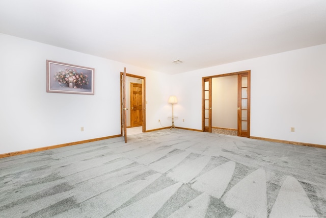 spare room with light colored carpet, french doors, and baseboards