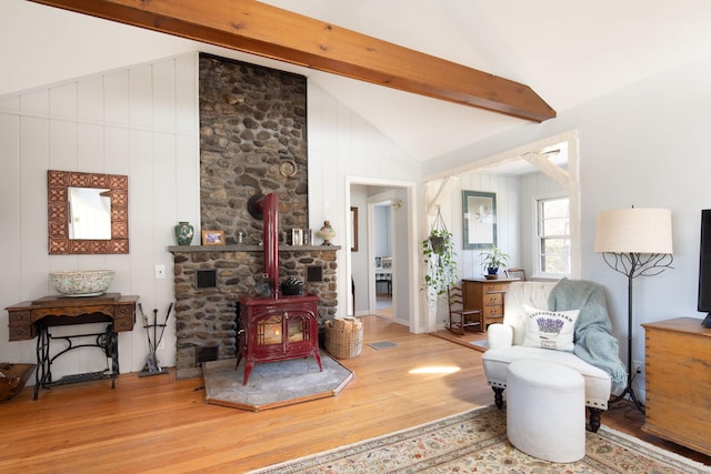 living area featuring visible vents, vaulted ceiling with beams, wood finished floors, and a wood stove