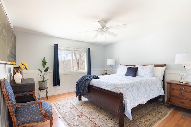 bedroom featuring ceiling fan, wood finished floors, and wainscoting