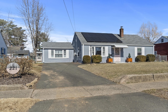 view of front of home featuring driveway, roof mounted solar panels, fence, roof with shingles, and a chimney