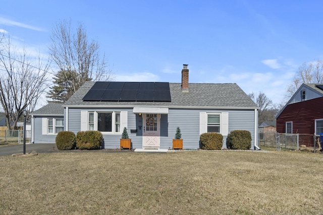 view of front of property with roof mounted solar panels, a chimney, a front lawn, and fence