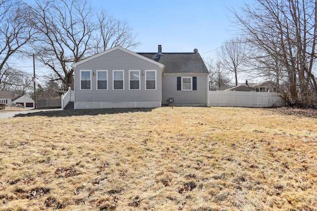 back of property with a shingled roof, a lawn, a chimney, and fence