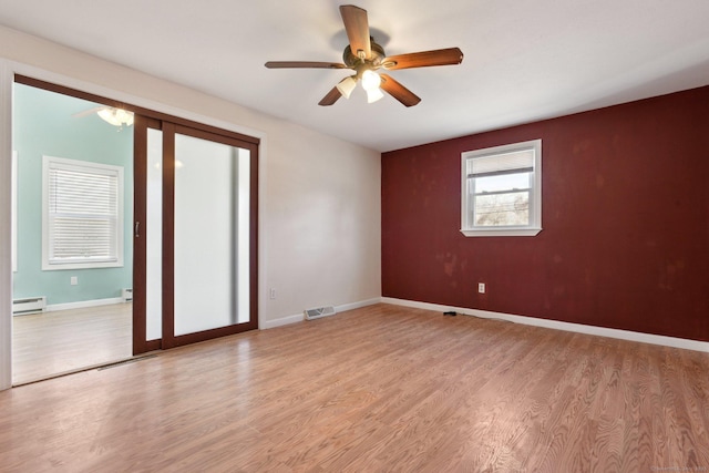 empty room featuring a baseboard heating unit, baseboards, light wood finished floors, and ceiling fan