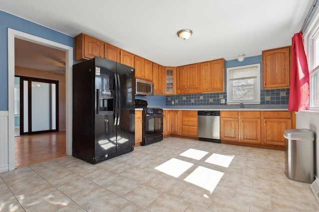 kitchen featuring backsplash, light countertops, brown cabinetry, black appliances, and a sink