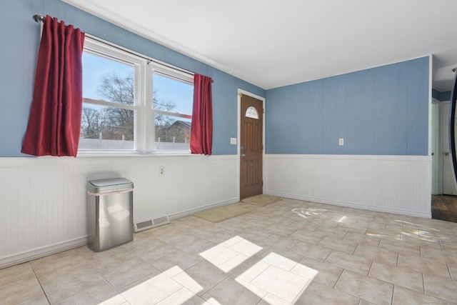 empty room with tile patterned floors, visible vents, and a wainscoted wall